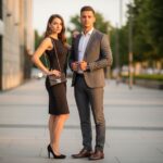 Stylowa para w eleganckich strojach stoi na tle miejskich świateł podczas złotej godziny.